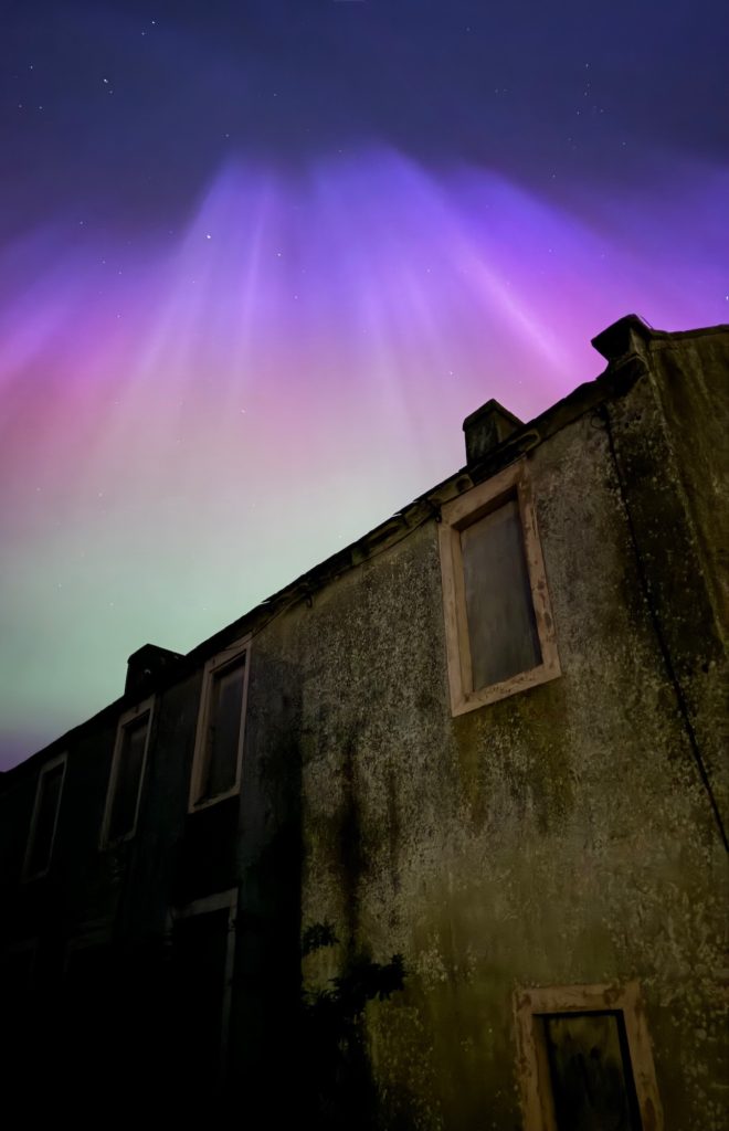 Northern lights in purple and green above a weathered stone building in Gilcrux at night